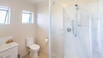 Un baño moderno con ducha envuelta en vidrio, inodoro y lavamanos con espejo.