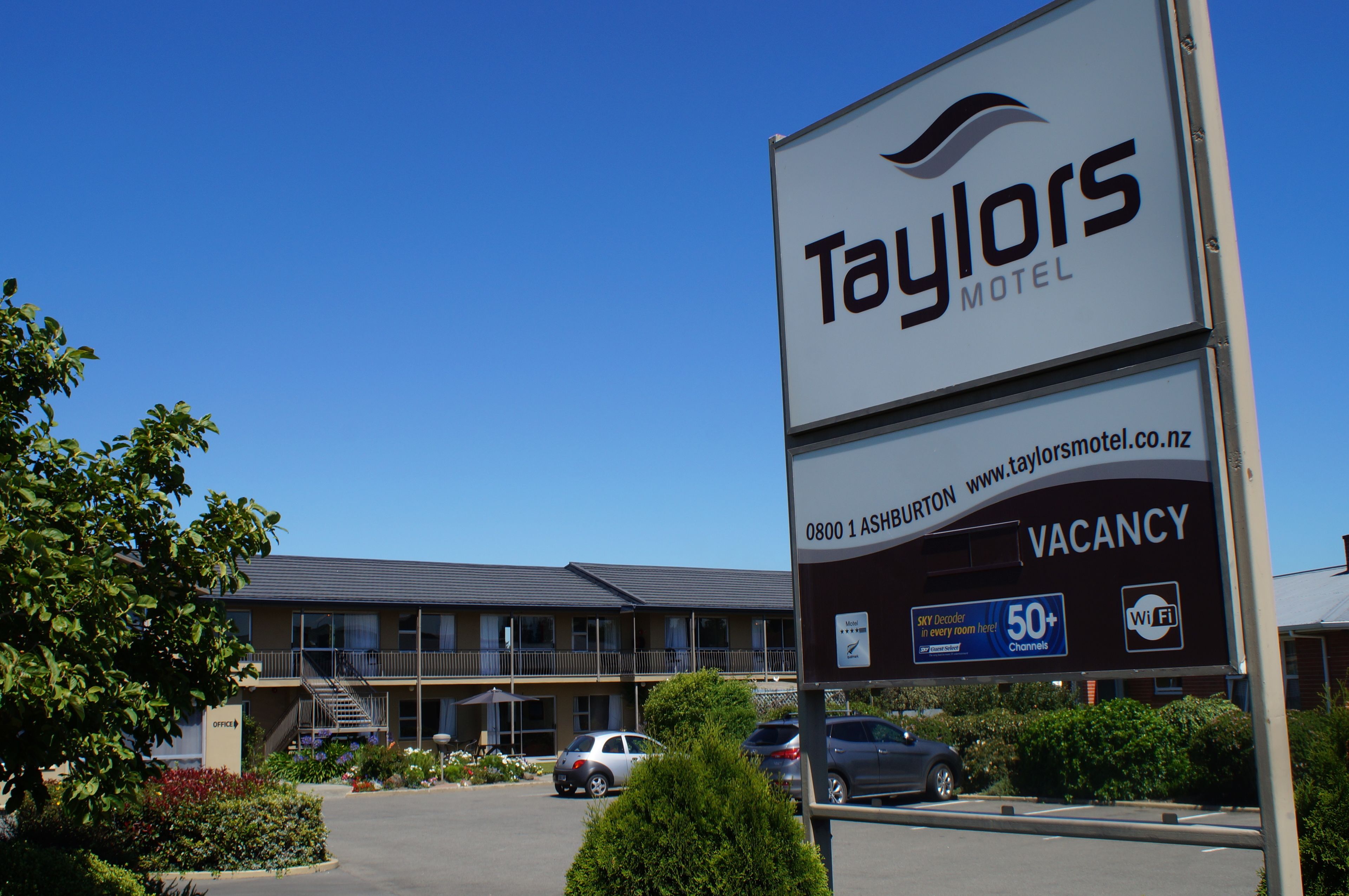 A TAYLORS MOTEL sign with a vacancy notice, a website URL, and amenities like 50+ channels and Wi-Fi.