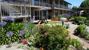 Un hotel con balcón, mobiliario exterior y un jardín con diversas plantas y flores.
