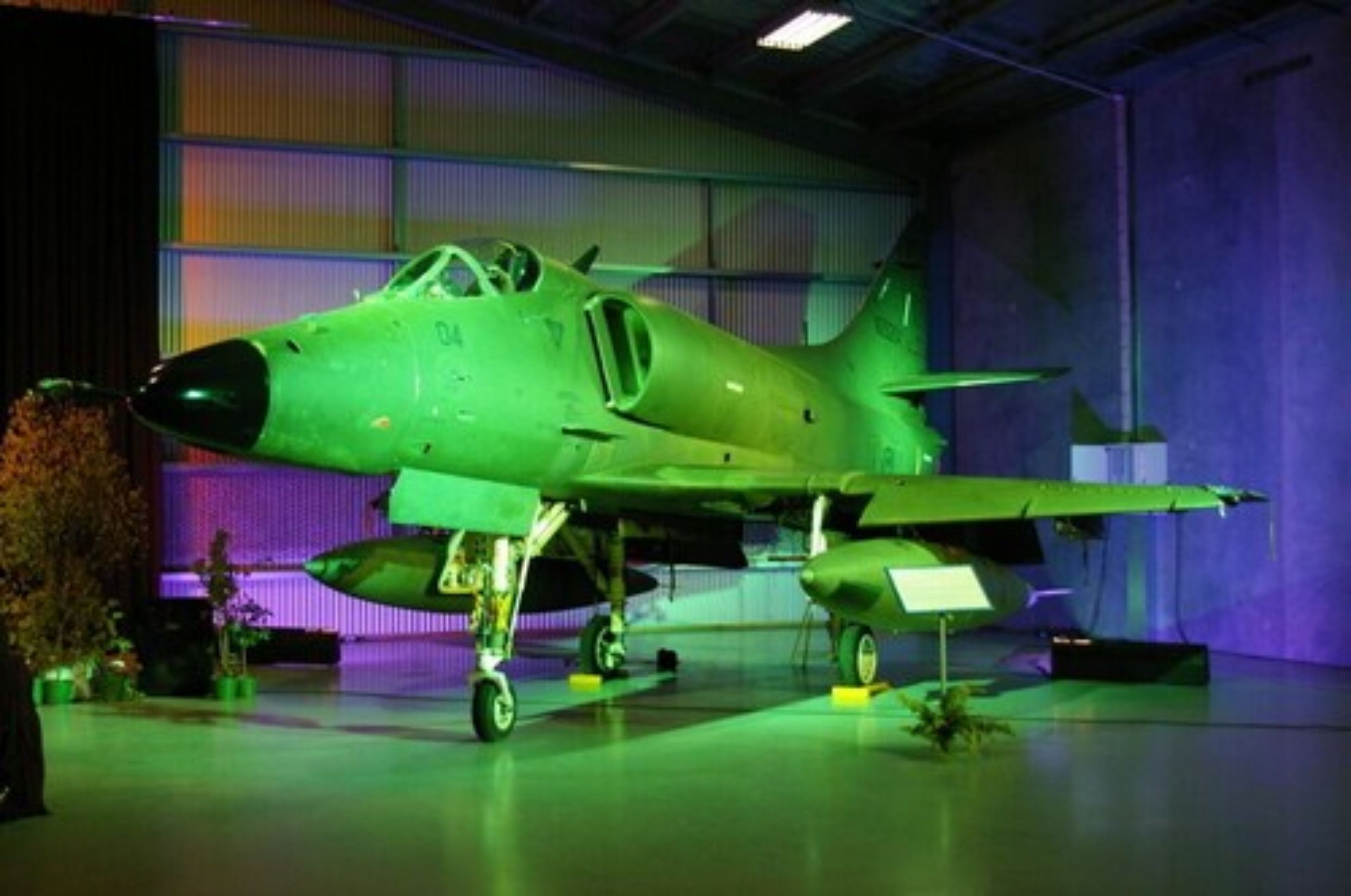 A green military aircraft on display in a hangar.