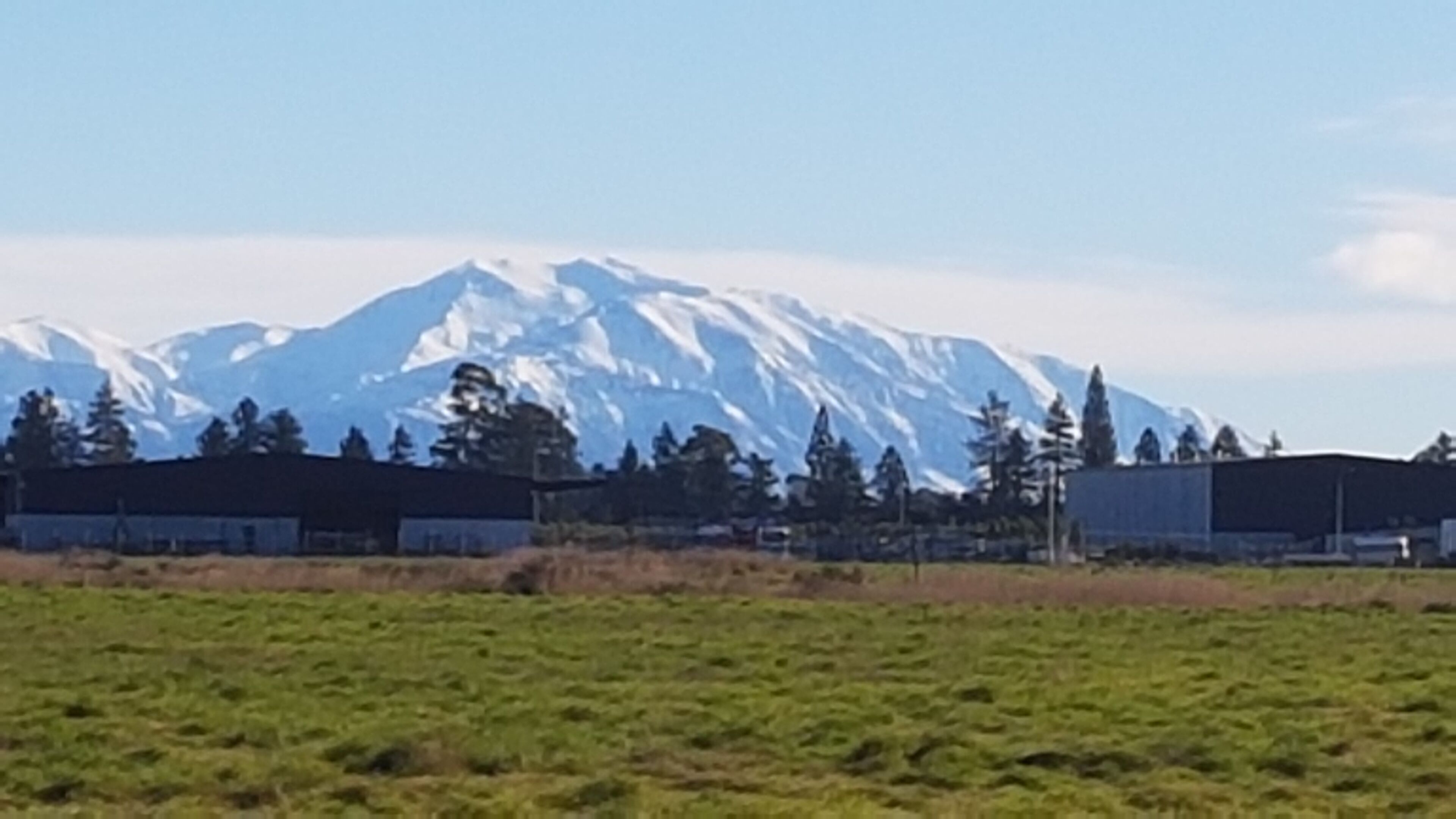 A mountainous landscape with snow-capped peaks, a grassy field, and several buildings in the foreground.