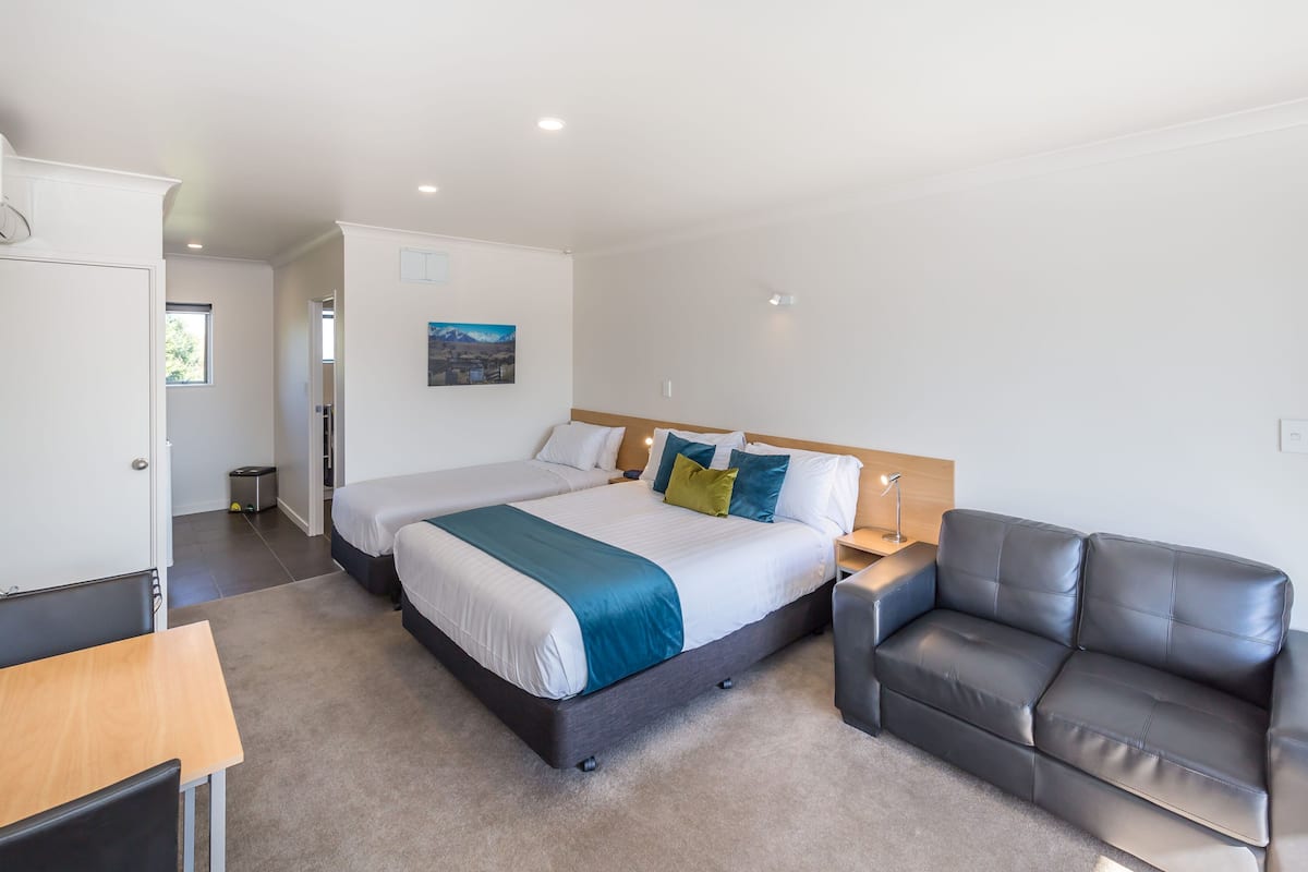 A modern hotel room with a large bed, a sofa, a desk, and a painting on the wall.