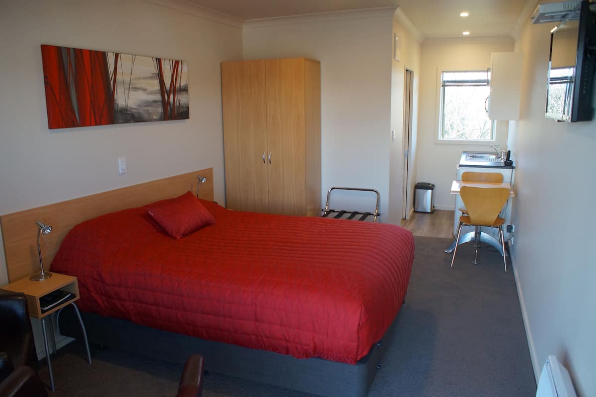 A hotel room with a large bed, a desk, a chair, and a wardrobe.