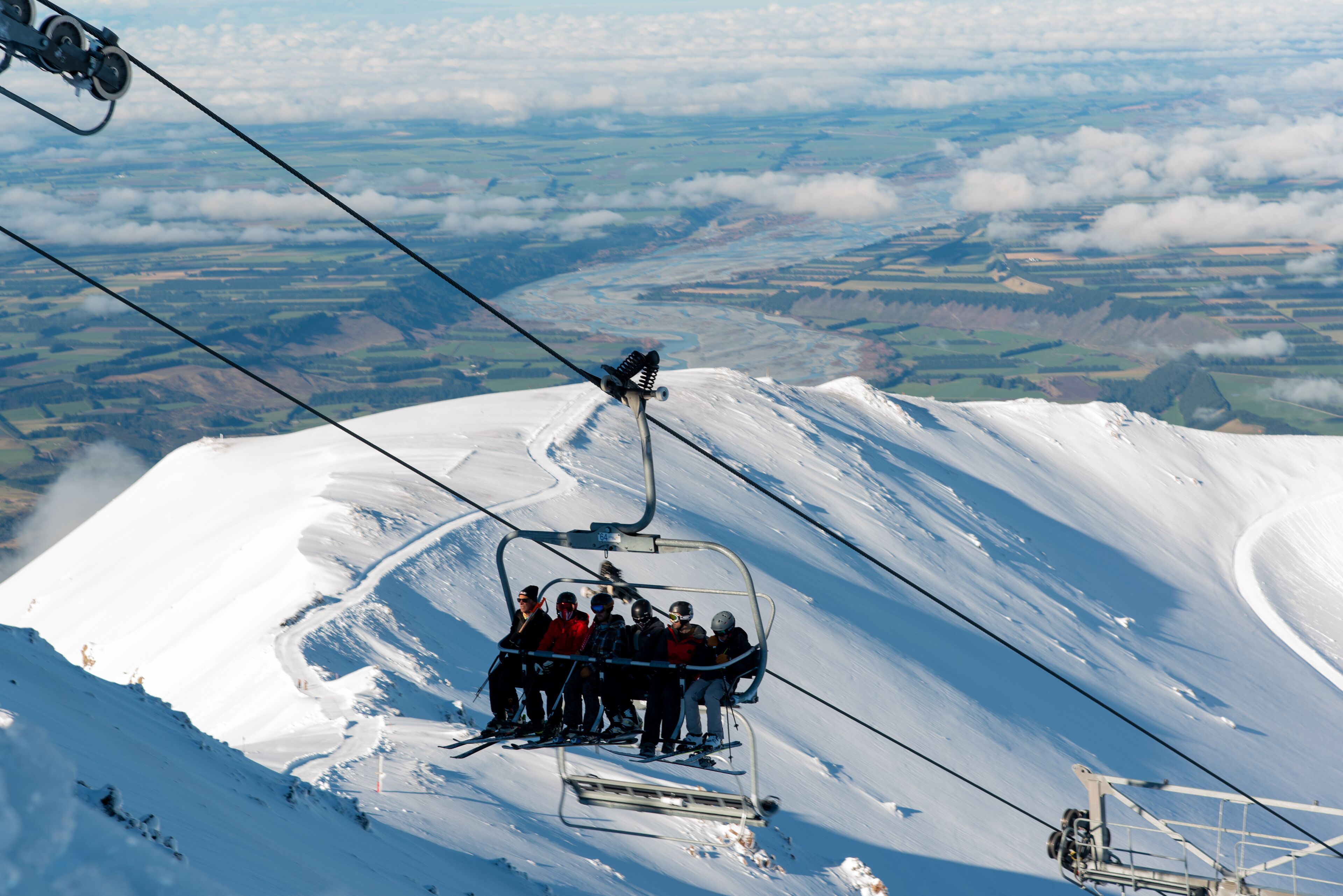 A ski lift with passengers ascending a snowy mountain.
