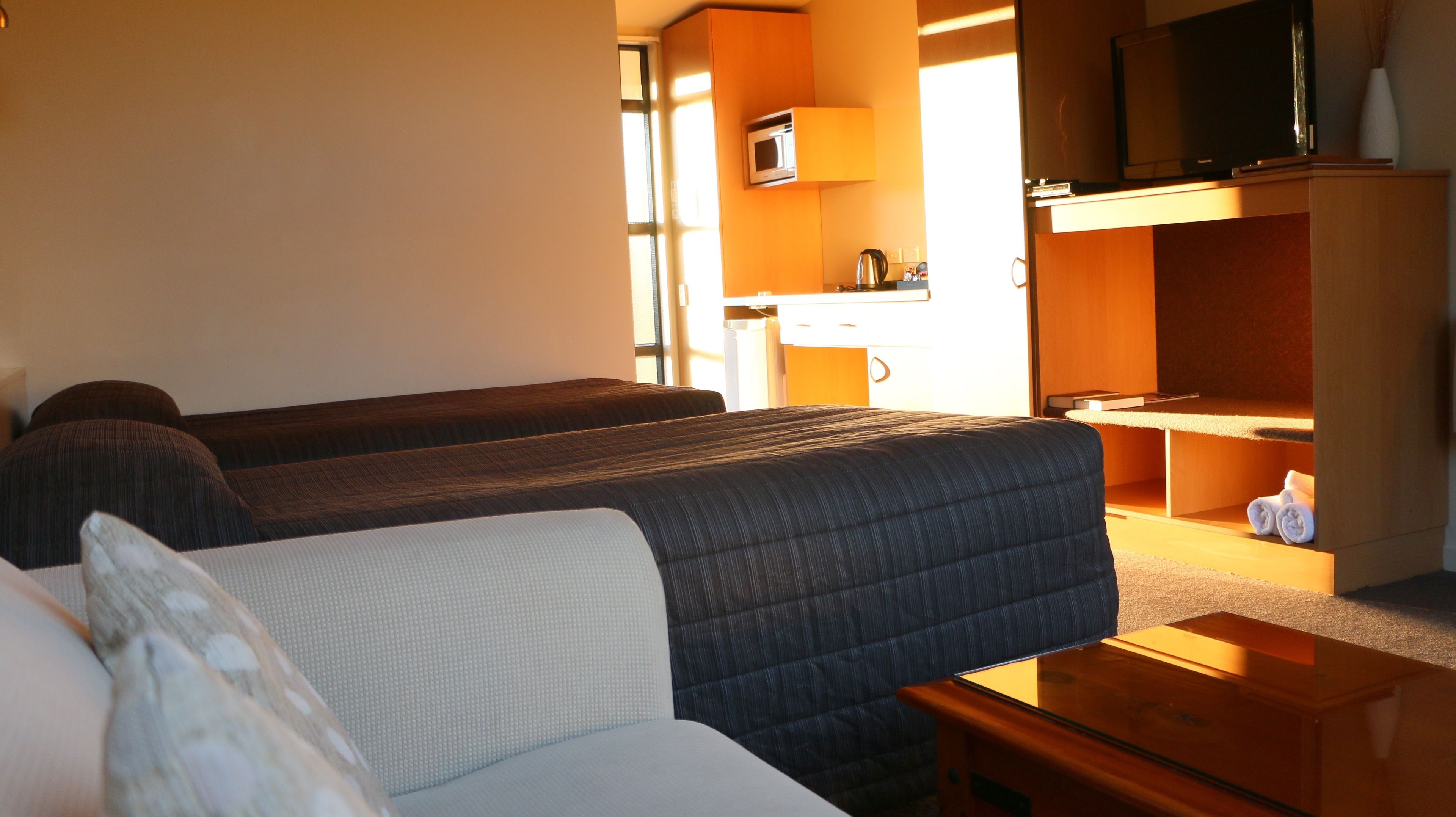 Habitación de hotel con dos camas, un sofá, un escritorio de madera, un televisor y un microondas.