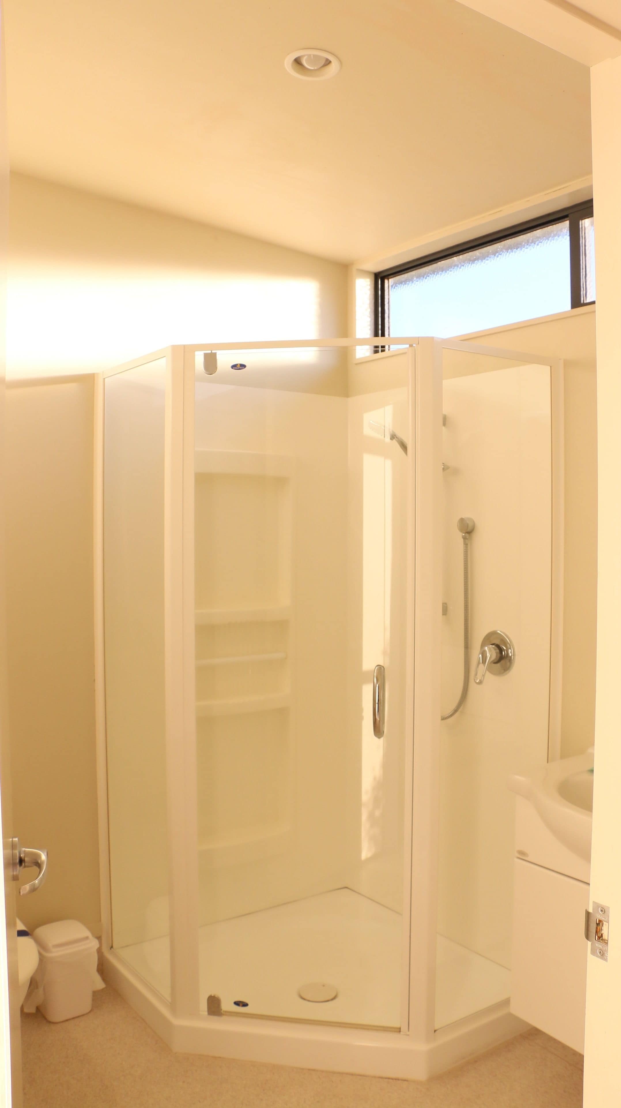 A corner bathroom with a glass-enclosed shower, a toilet, and a sink.