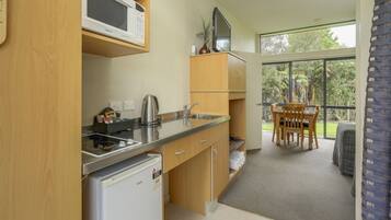 A compact kitchen with a microwave, kettle, and a small refrigerator. There is a dining area with a table and chairs, and a large window offering a view of the outdoors.