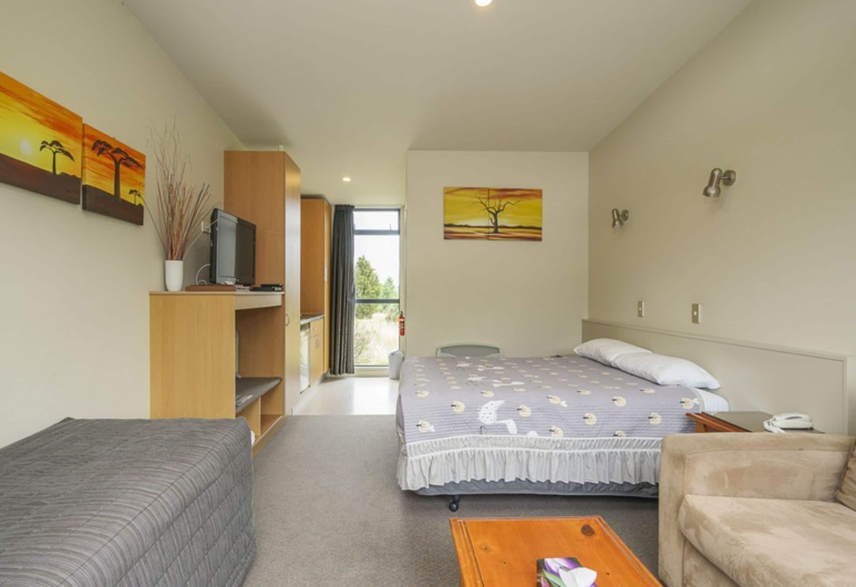 Ein Hotelzimmer mit Bett, Sofa, Fernseher und Bildern an den Wänden.
