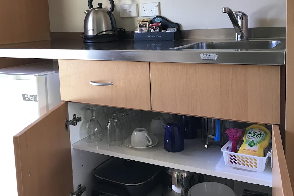 A compact kitchenette with a kettle, a coffee maker, a sink, and a small refrigerator.