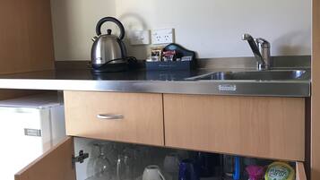 Een kleine keuken met een waterkoker, een koffiezetapparaat, een spoelbak en een kleine koelkast.
