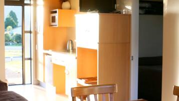 Un comedor con mesa y sillas de madera, una cocina con microondas y armarios, y un televisor montado sobre los armarios.