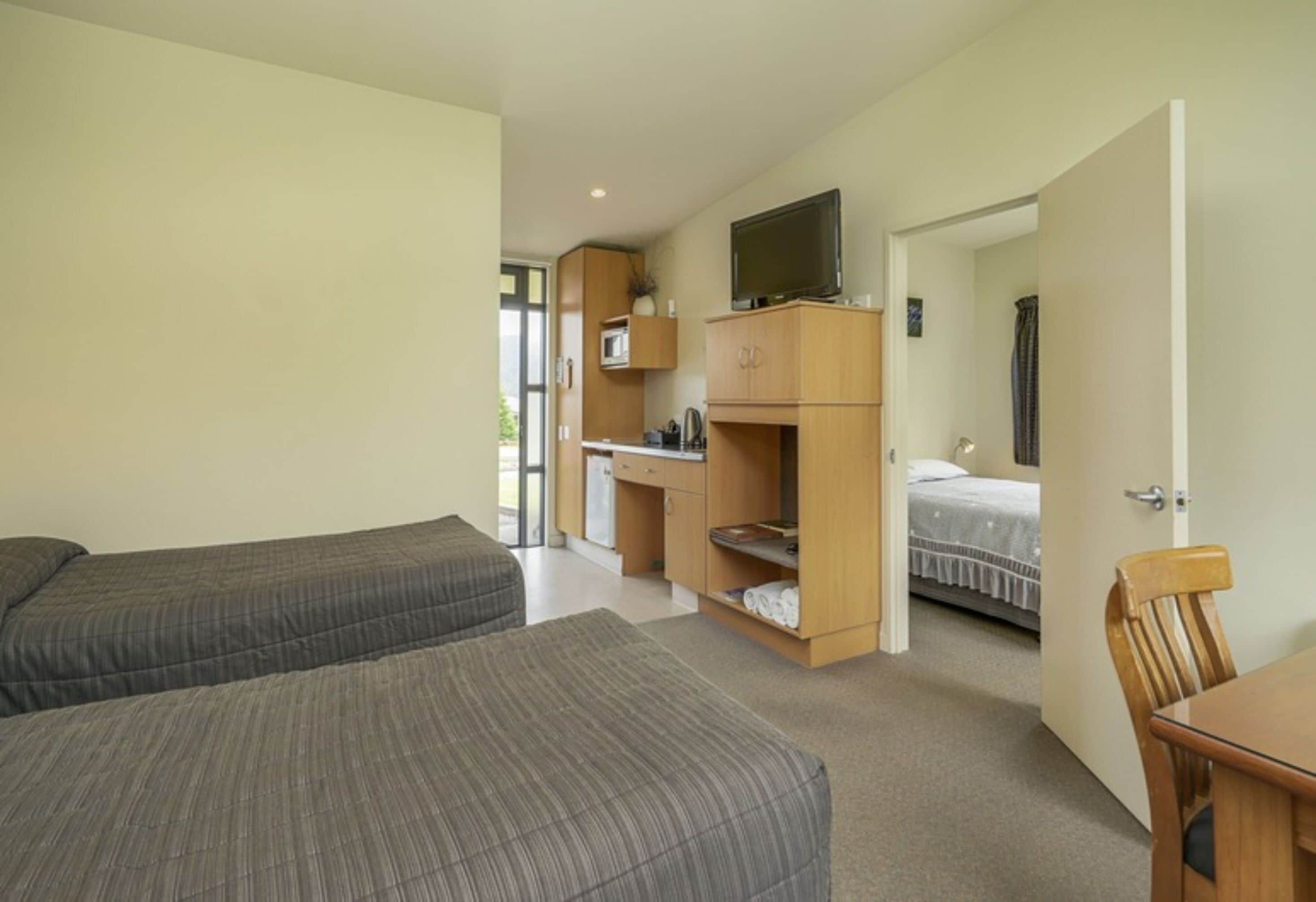 A compact room with two beds, a desk, a television, and a small kitchenette.