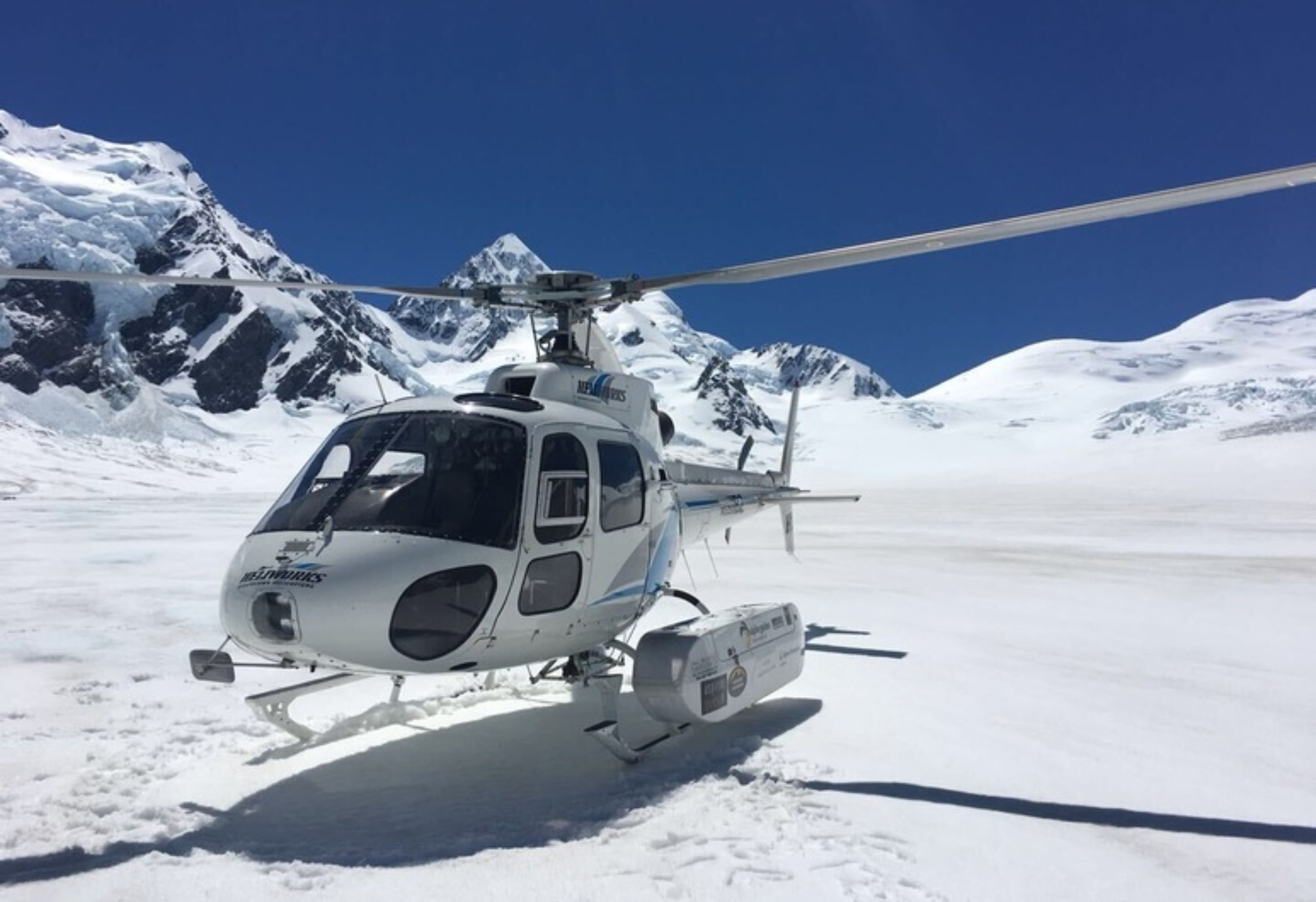 A helicopter parked on snow with mountains in the background.