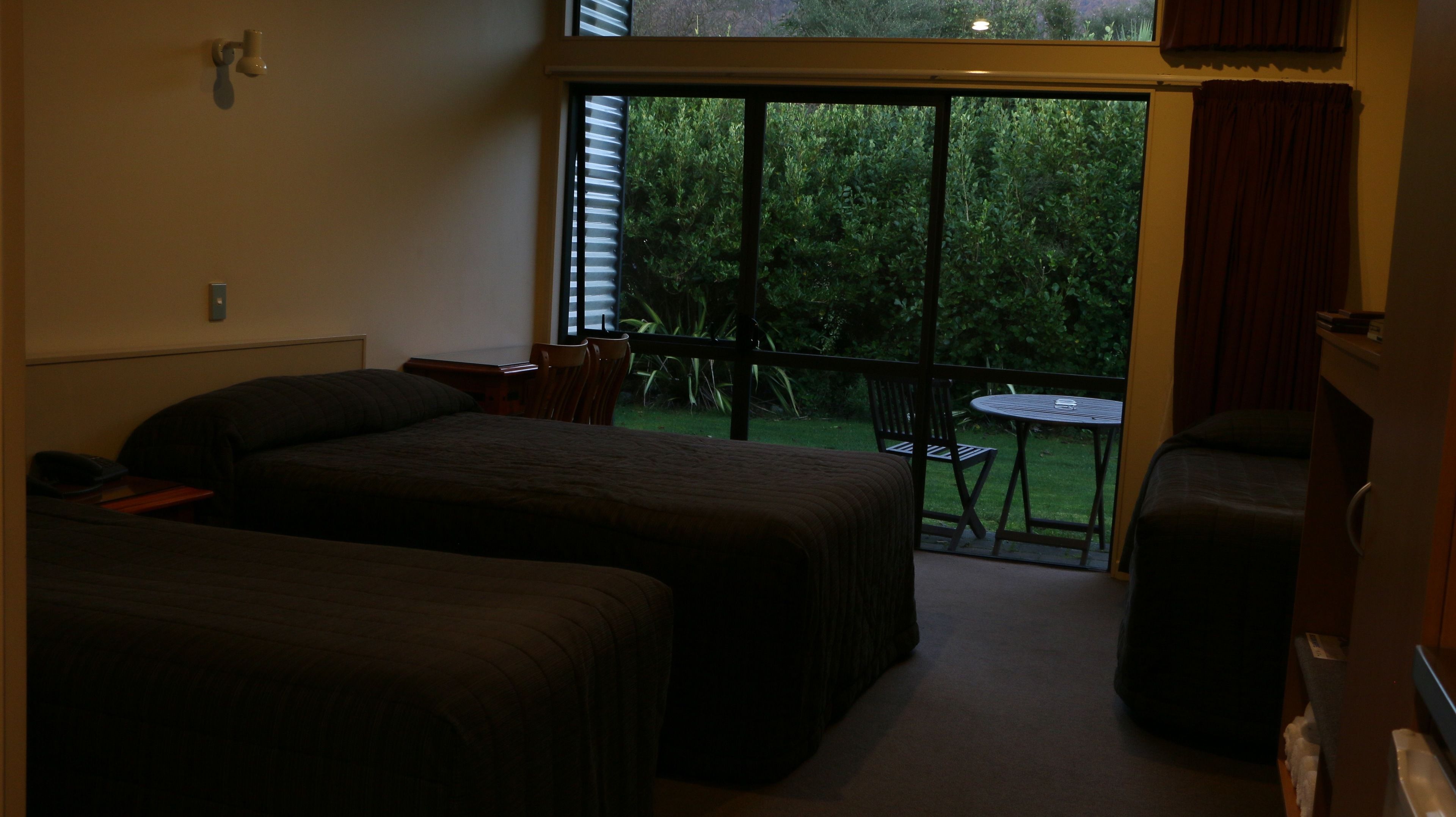 Ein Hotelzimmer mit zwei Betten, einem kleinen Tisch und Blick auf einen Garten durch eine Schiebetür.