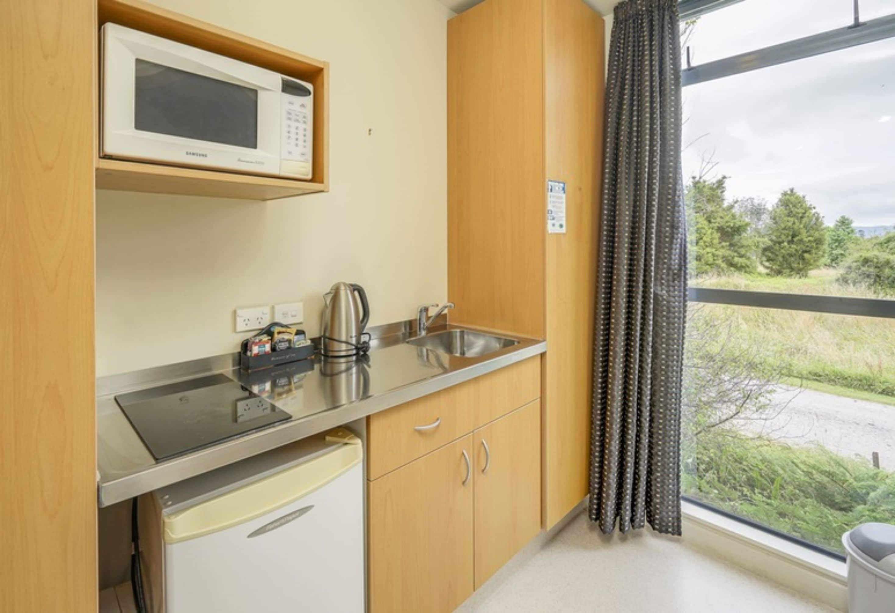 Een kleine keuken met een magnetron, waterkoker en gootsteen.