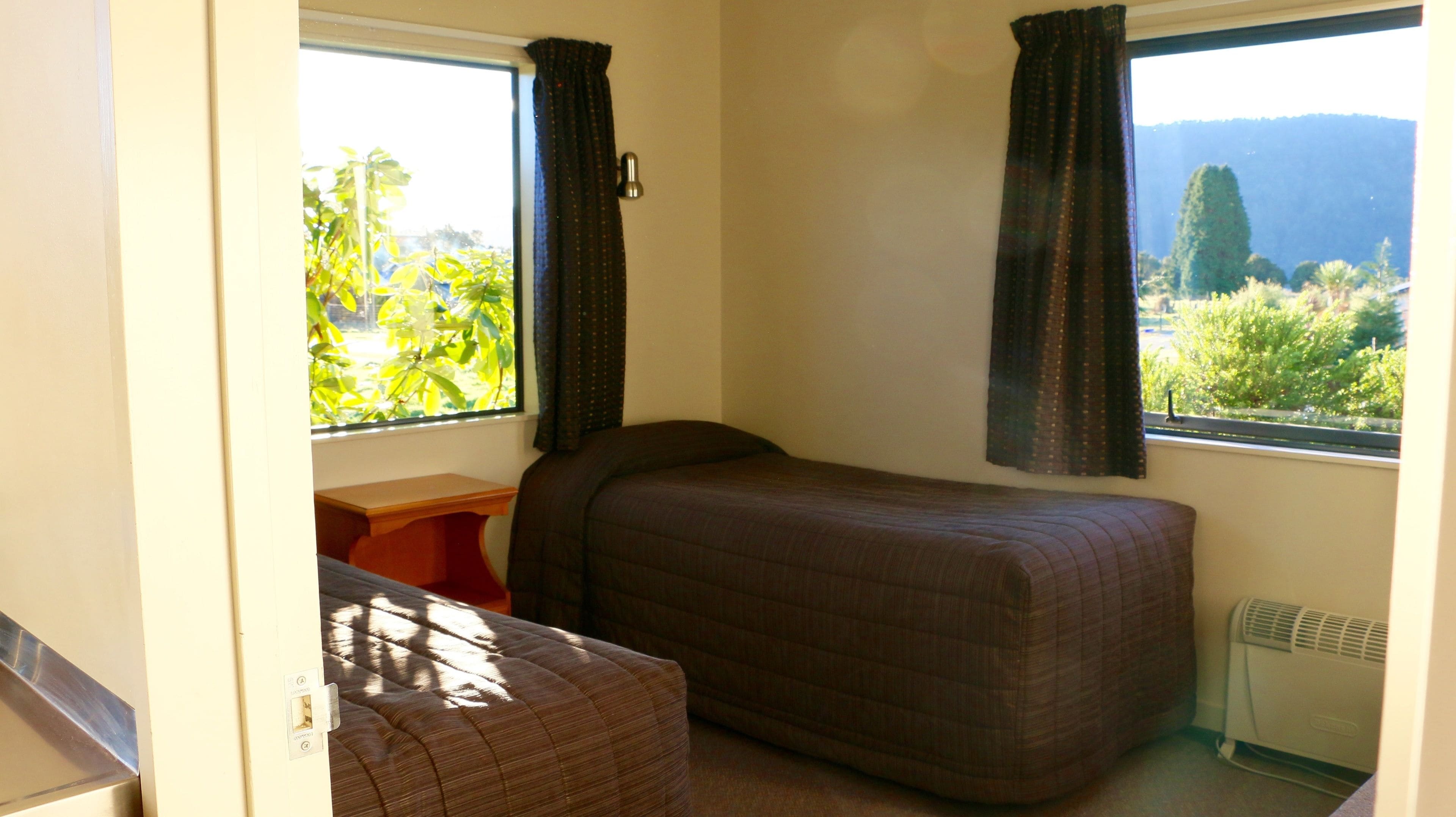 A small, single-bed room with a window providing a view of greenery and hills.
