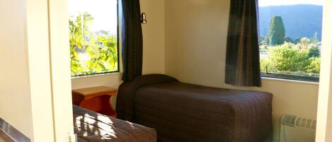 A small, single-bed room with a window providing a view of greenery and hills.