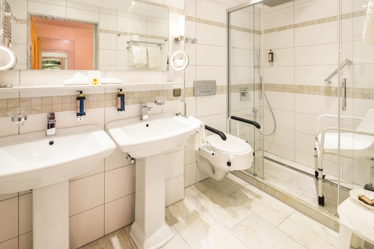 Une salle de bain moderne avec deux lavabos, des toilettes et une douche séparée par une paroi de verre.
