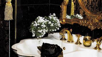 Un baño lujoso con un lavamanos blanco, grifos dorados y un espejo grande y ornamentado.