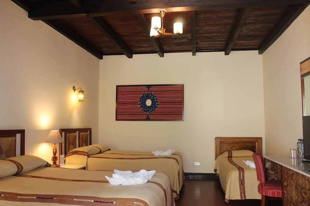 Habitación de hotel con dos camas, techo de madera, lámpara fijada a la pared y una obra de arte enmarco.
