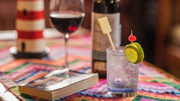 Una mesa con un libro, una copa de vino tinto, una botella de vino y un cóctel adornado con una rodaja de lima.