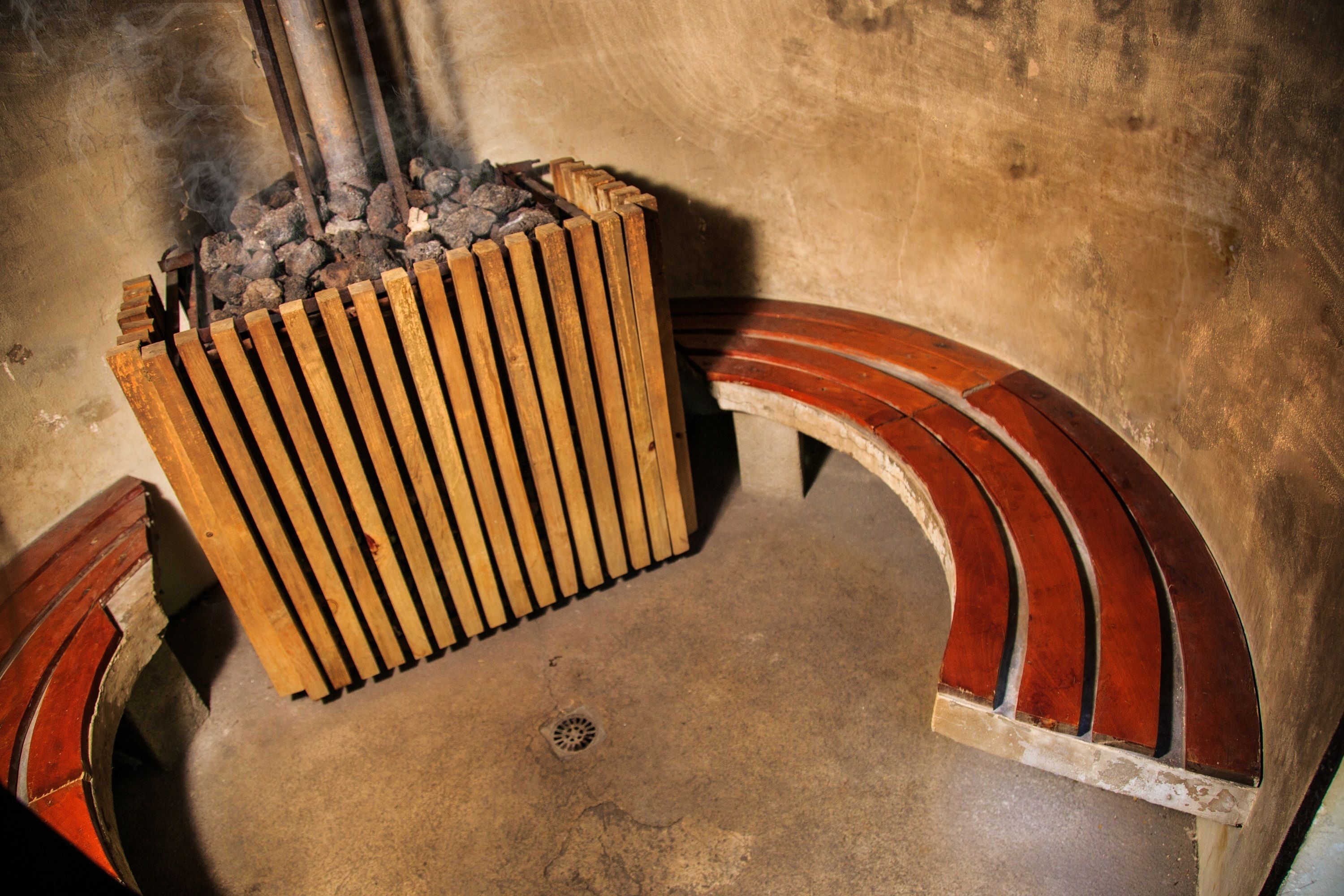 Un banc en bois au design incurvé, un sol en béton et une grille métallique sur laquelle brûlent des charbons ardents.
