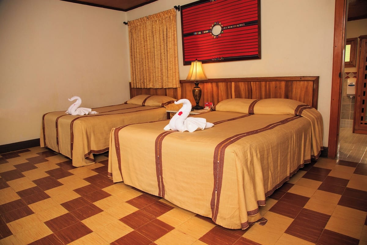 Habitación de hotel con dos camas, piso a cuadros, un adorno rojo en la pared y una lámpara.