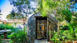 Una construcción de piedra con una puerta, rodeada de exuberante vegetación y un sendero adoquinado.