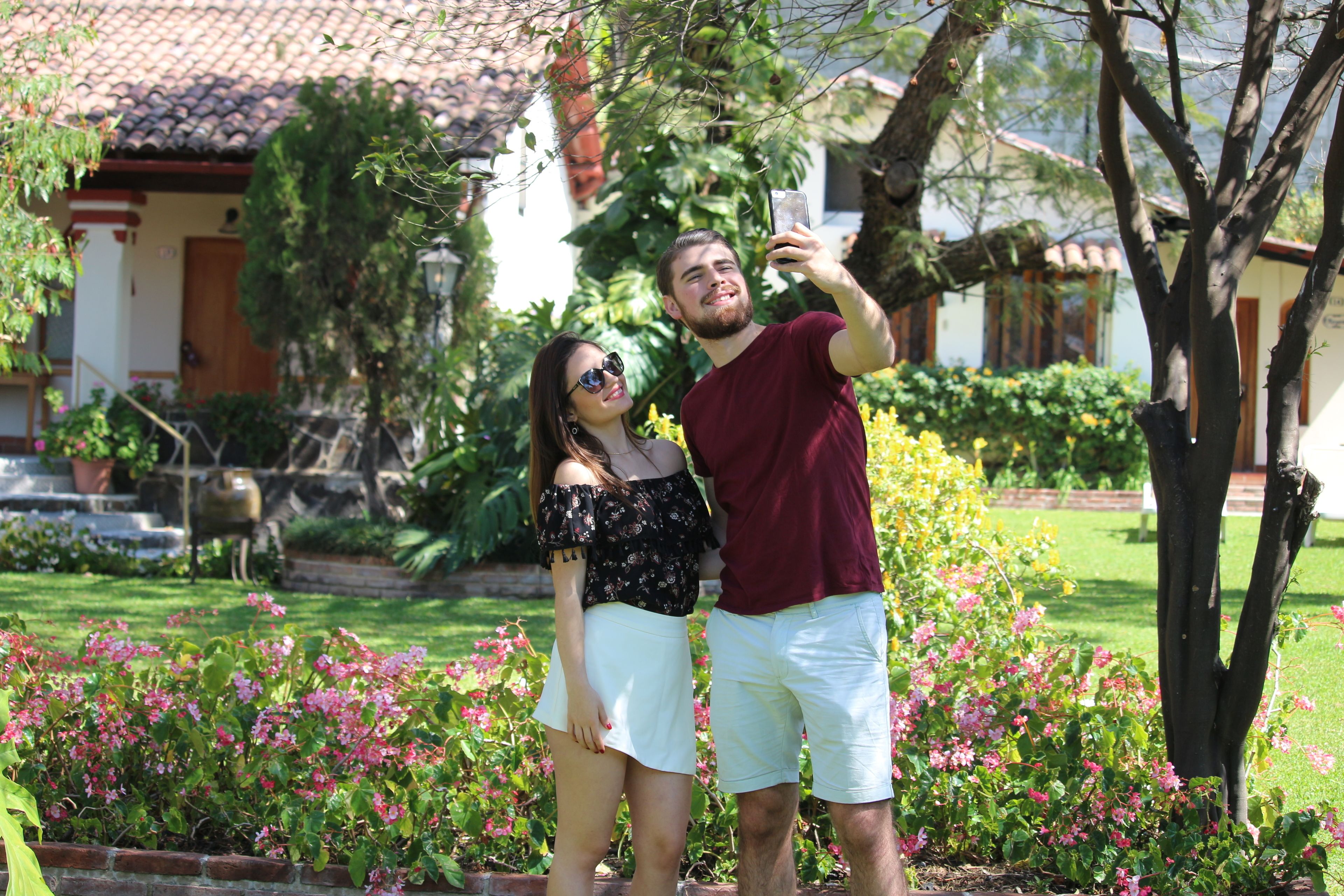 A couple taking a selfie in a garden with a house in the background.