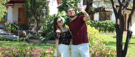 A couple taking a selfie in a garden with a house in the background.