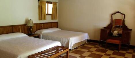 A room with two beds, a wooden bench, a desk with a mirror, and a checkered floor.