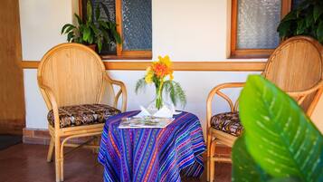 Una habitación con dos sillones de mimbre, una mesita con mantel a rayas de colores y un jarrón con flores.