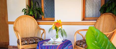 Una habitación con dos sillones de mimbre, una mesita con mantel a rayas de colores y un jarrón con flores.