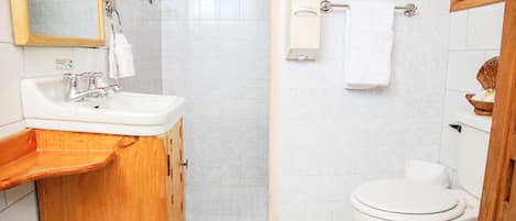 Un baño con tocador de madera, lavabo blanco, espejo, inodoro y barra para toallas.