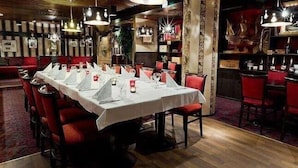 Un restaurant avec une longue table dressée pour un repas, des chaises rouges et des lampes suspendues.
