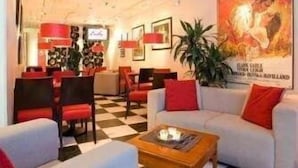 Un hall d’hôtel avec un sol à carreaux, un canapé avec des coussins rouges, une table basse en bois et une affiche accrochée au mur.