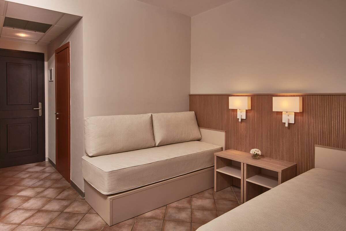 Ein modernes Hotelzimmer mit einer Couch, einem kleinen Holztisch und zwei Wandleuchten.