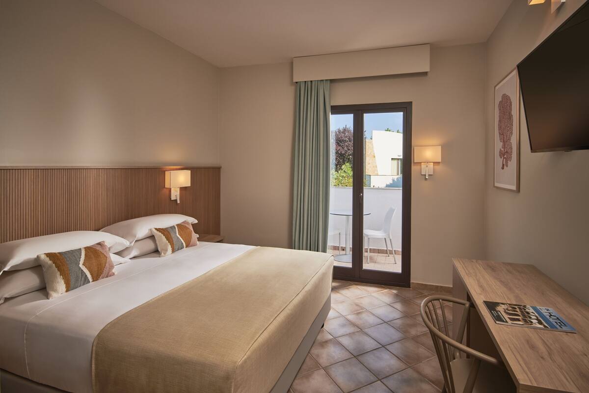 Ein Hotelzimmer mit Bett, Schreibtisch, Sessel, Fernseher und einem Balkon mit Blick.
