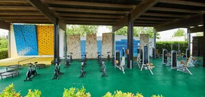 An outdoor gym with stationary bikes, treadmills, and weight machines under a covered area with a green floor. - Torreserena Resort (Ginosa)