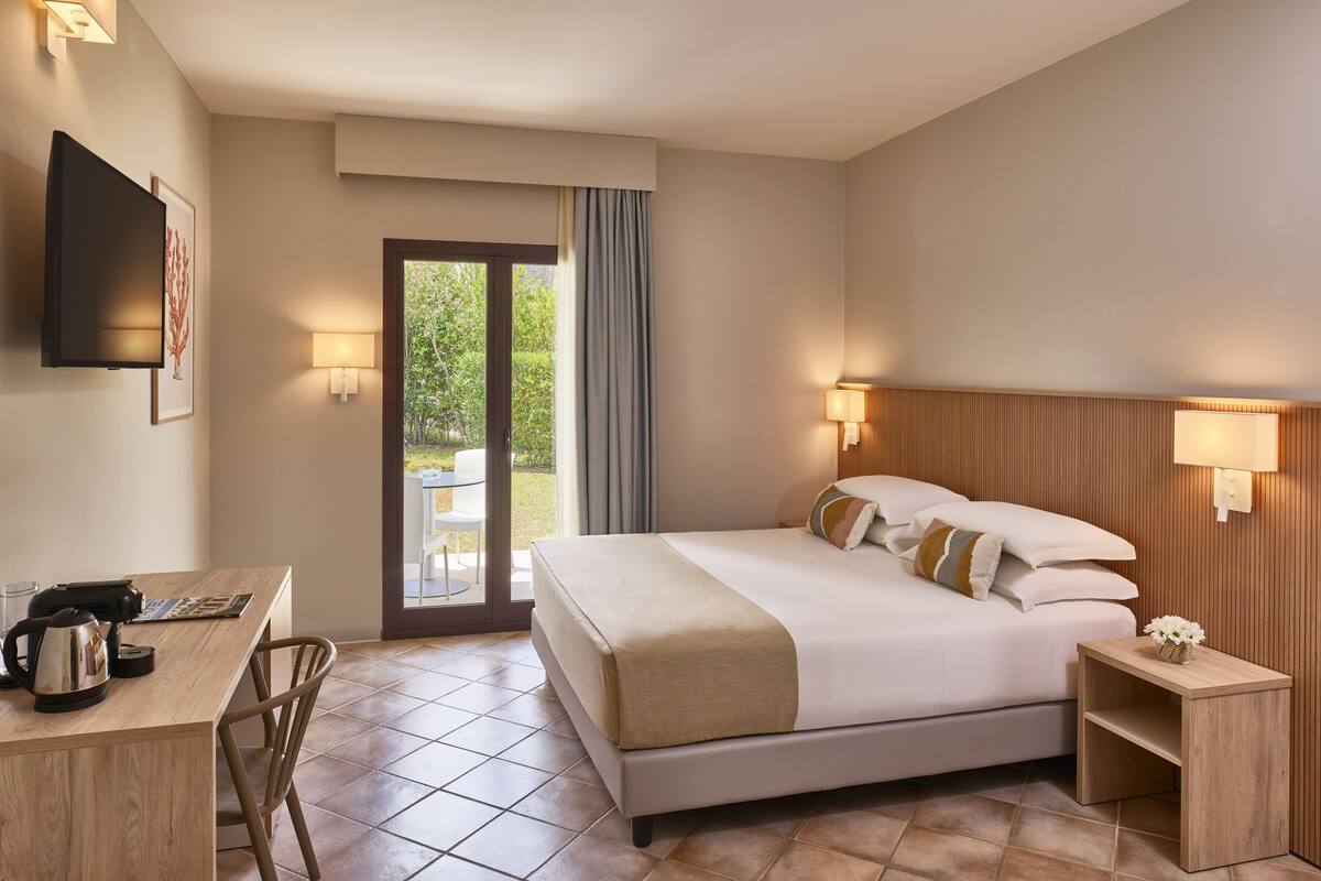 Ein Hotelzimmer mit Bett, Nachttisch, Schreibtisch, Stuhl und einem an der Wand befestigten Fernseher.