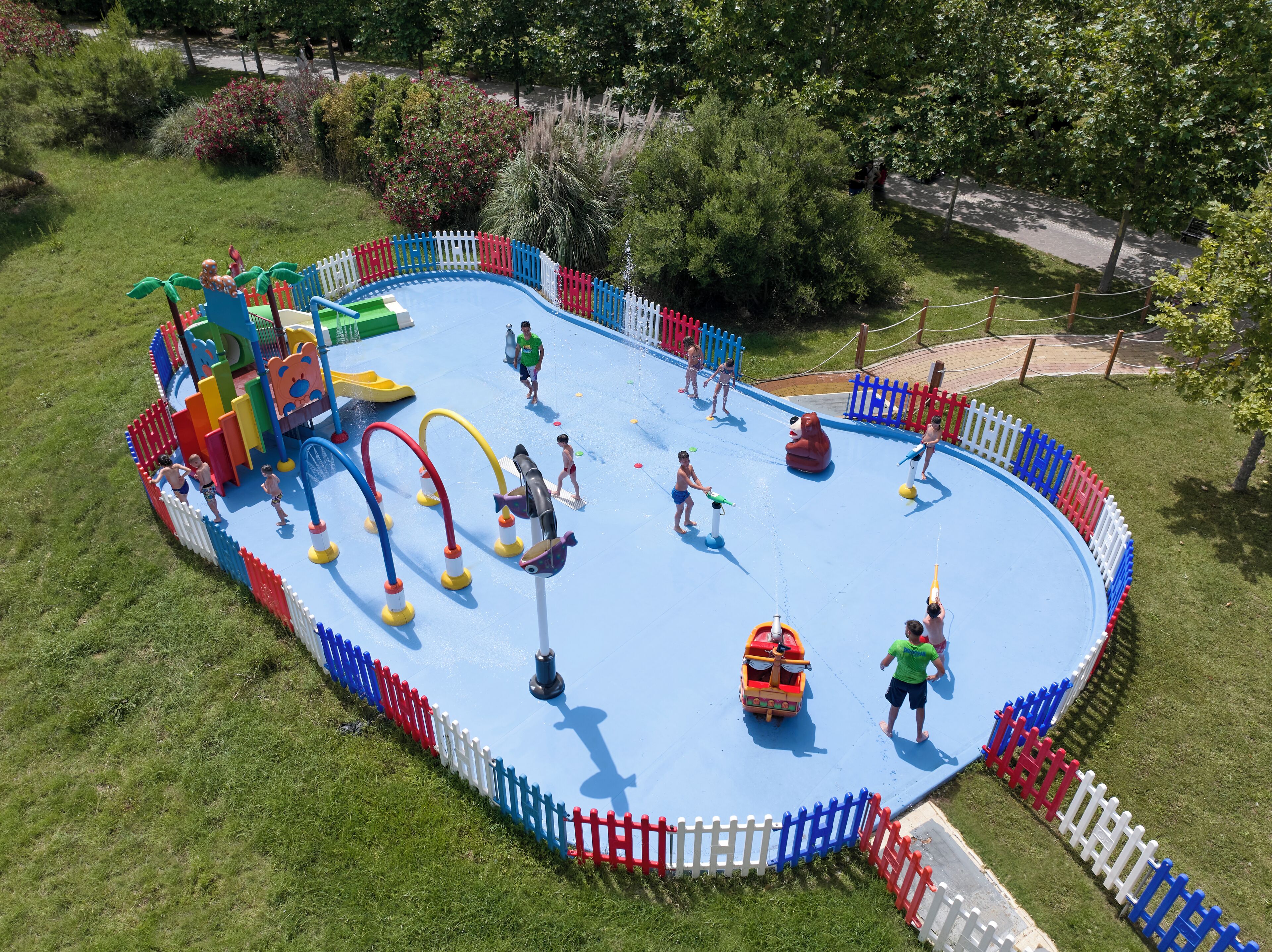 Un parco acquatico con piscina azzurra, strutture ludiche e un’area recintata.