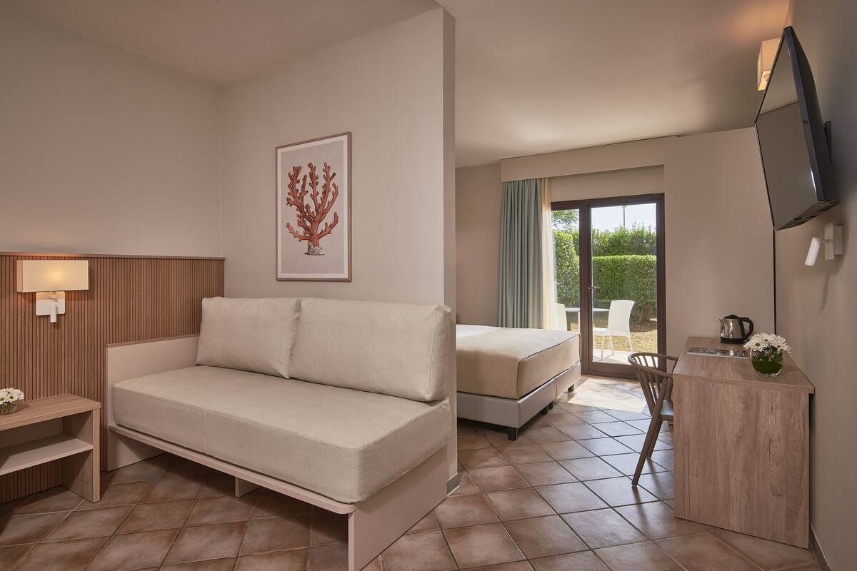 Ein modernes Hotelzimmer mit einer Couch, einem Bett, einem kleinen Schreibtisch, einem Fernseher und einem Balkon mit Blick.