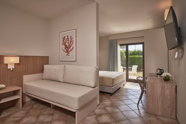 Una habitación de hotel moderna con sofá, cama, escritorio pequeño, televisor y balcón con vistas.