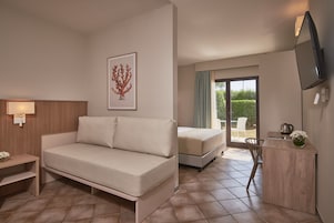 Una habitación de hotel moderna con sofá, cama, escritorio pequeño, televisor y balcón con vistas.