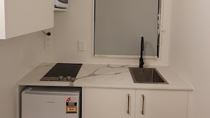 A compact kitchen with a built-in microwave, a small refrigerator, a sink, and a window above the sink.
