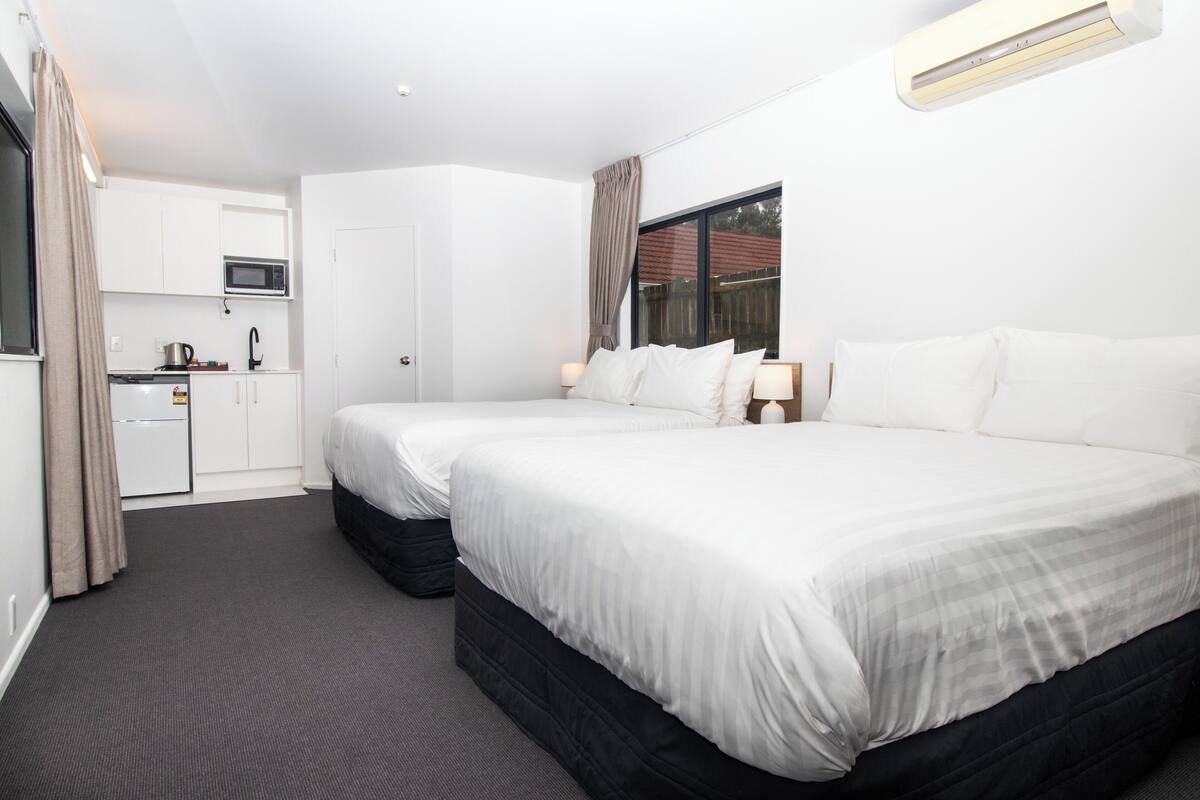 A hotel room with two beds, a kitchenette, and a window with curtains.