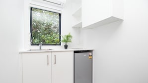 A modern kitchen with white cabinets, a built-in dishwasher, a window with a view of greenery, and a potted plant on the counter.