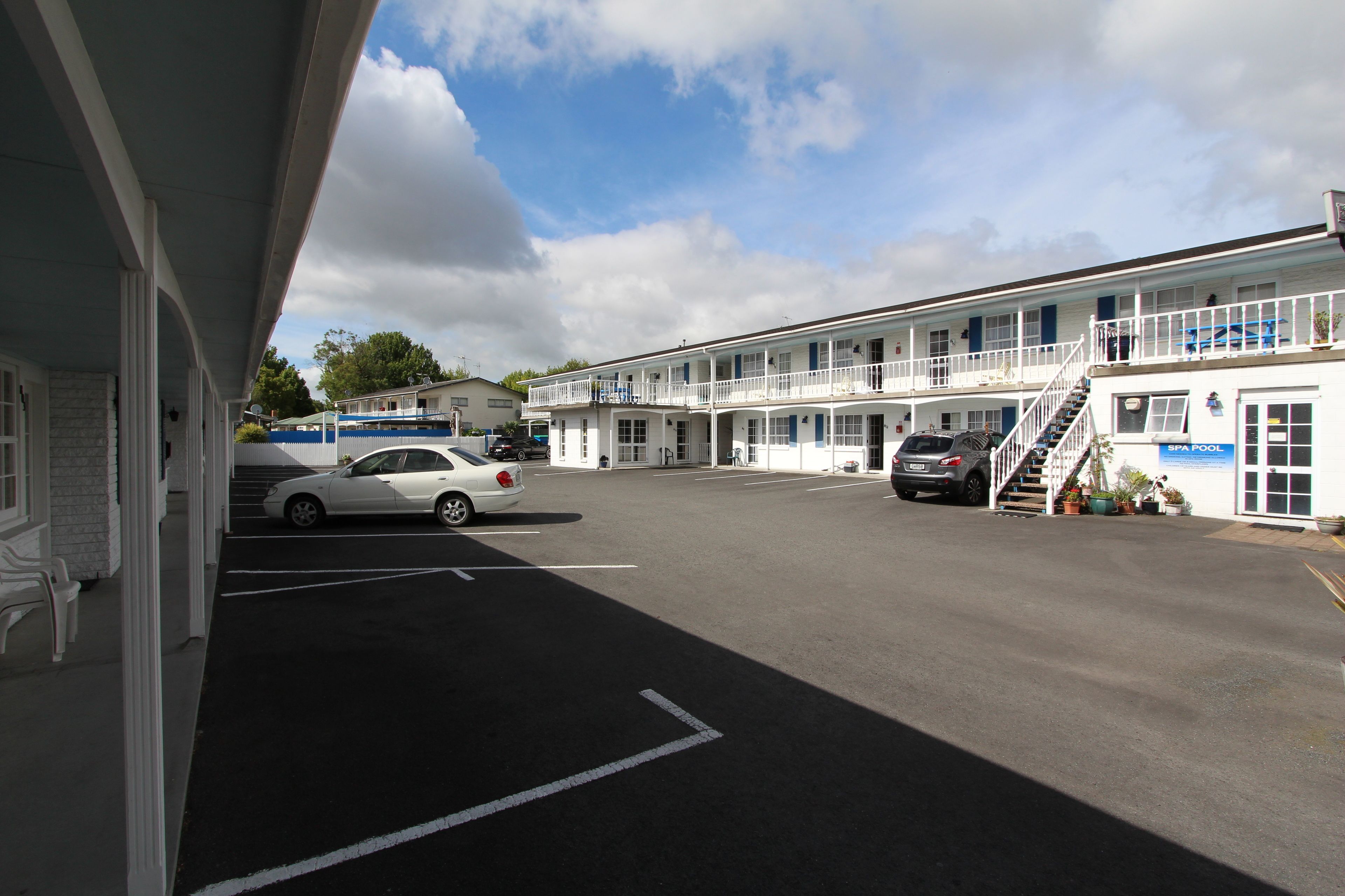 Een motel met een overdekte parkeerplaats, meerdere kamers en een trap naar de bovenverdieping.