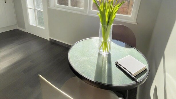 A room with a round glass table, a white chair, and a vase with white flowers. - Boundary Court Motor Inn (Hamilton)