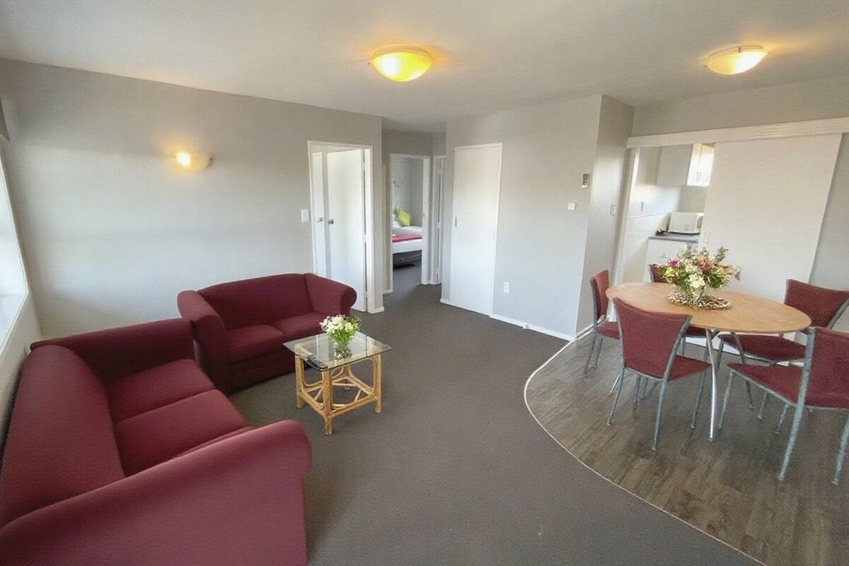 A modern living room with a red sofa set, a glass coffee table, and a dining area with a wooden table and red chairs.
